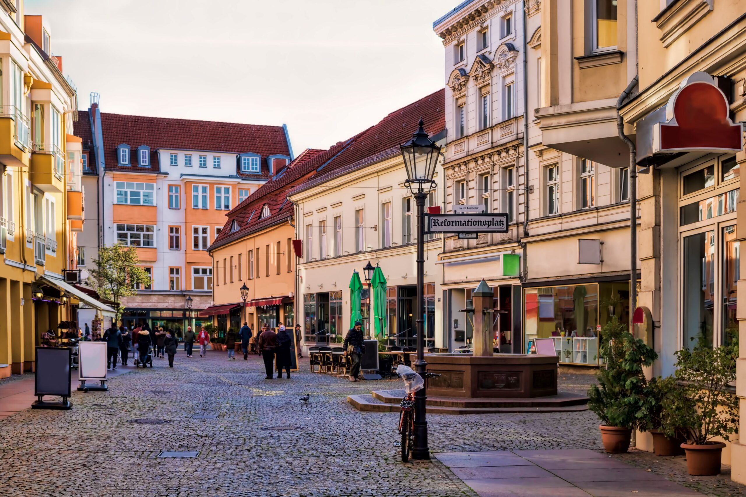 Ein Brunnen in einer Altstadt mit verschiedenen Restaurants und Personen 